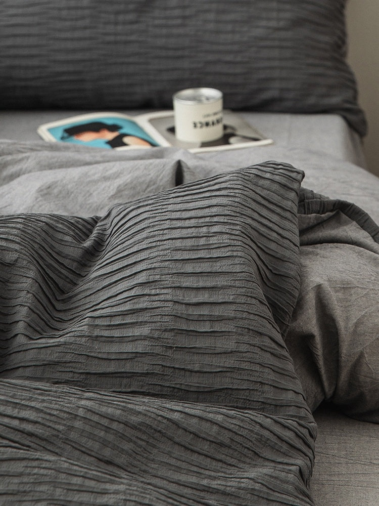 Gray textured bedding on a bed with a magazine and candle on a nightstand.