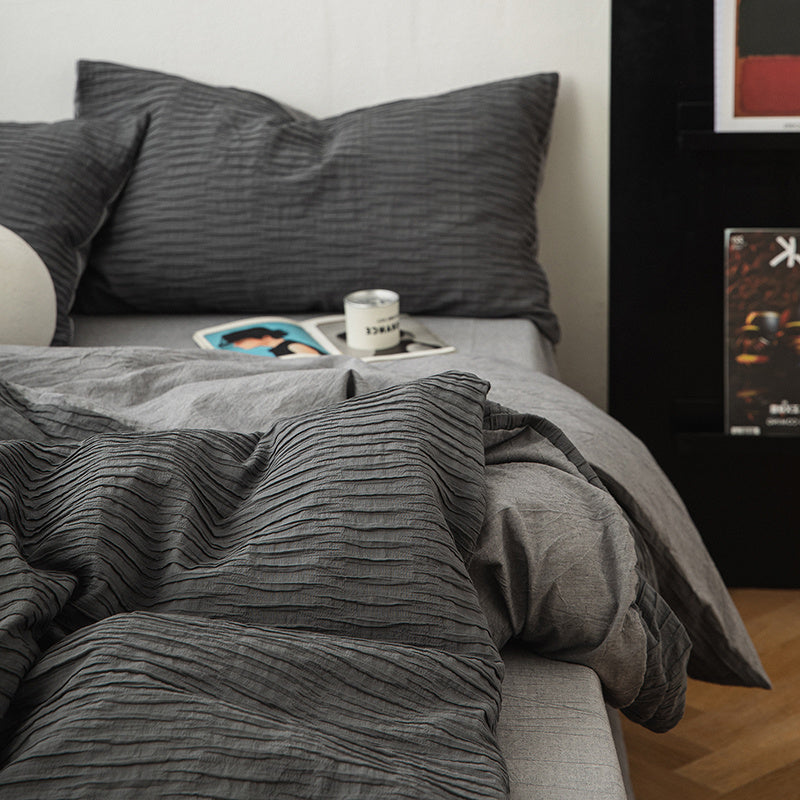 Gray bedding set on a bed with pillows and a small table.