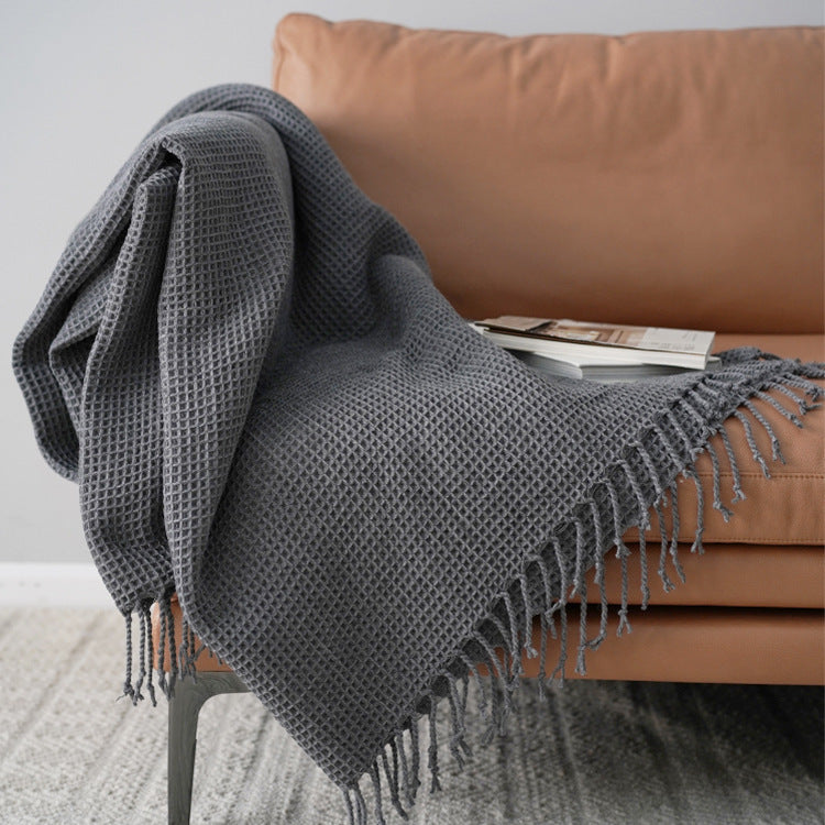 Gray textured throw blanket draped over a brown sofa with a white wall background