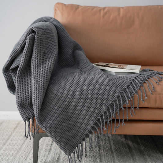 Gray textured throw blanket draped over a brown sofa with a white wall background